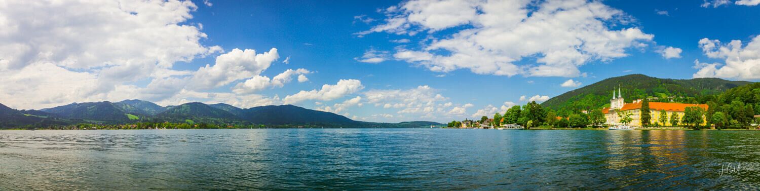 A lake with mountains in the background and a building with a red roof on the right.