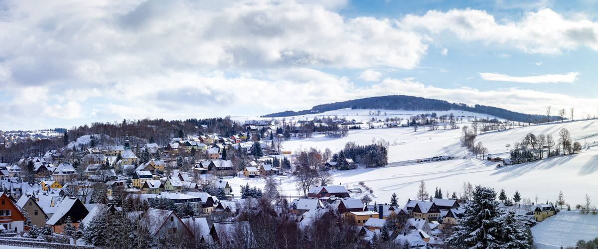 A snow-covered village with houses, a church, and a hill in the background.
