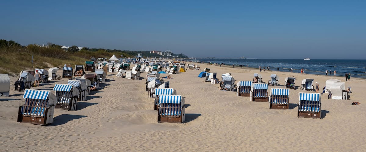 A beach with rows of beach chairs and umbrellas, a sandy shore, and the ocean in the background.