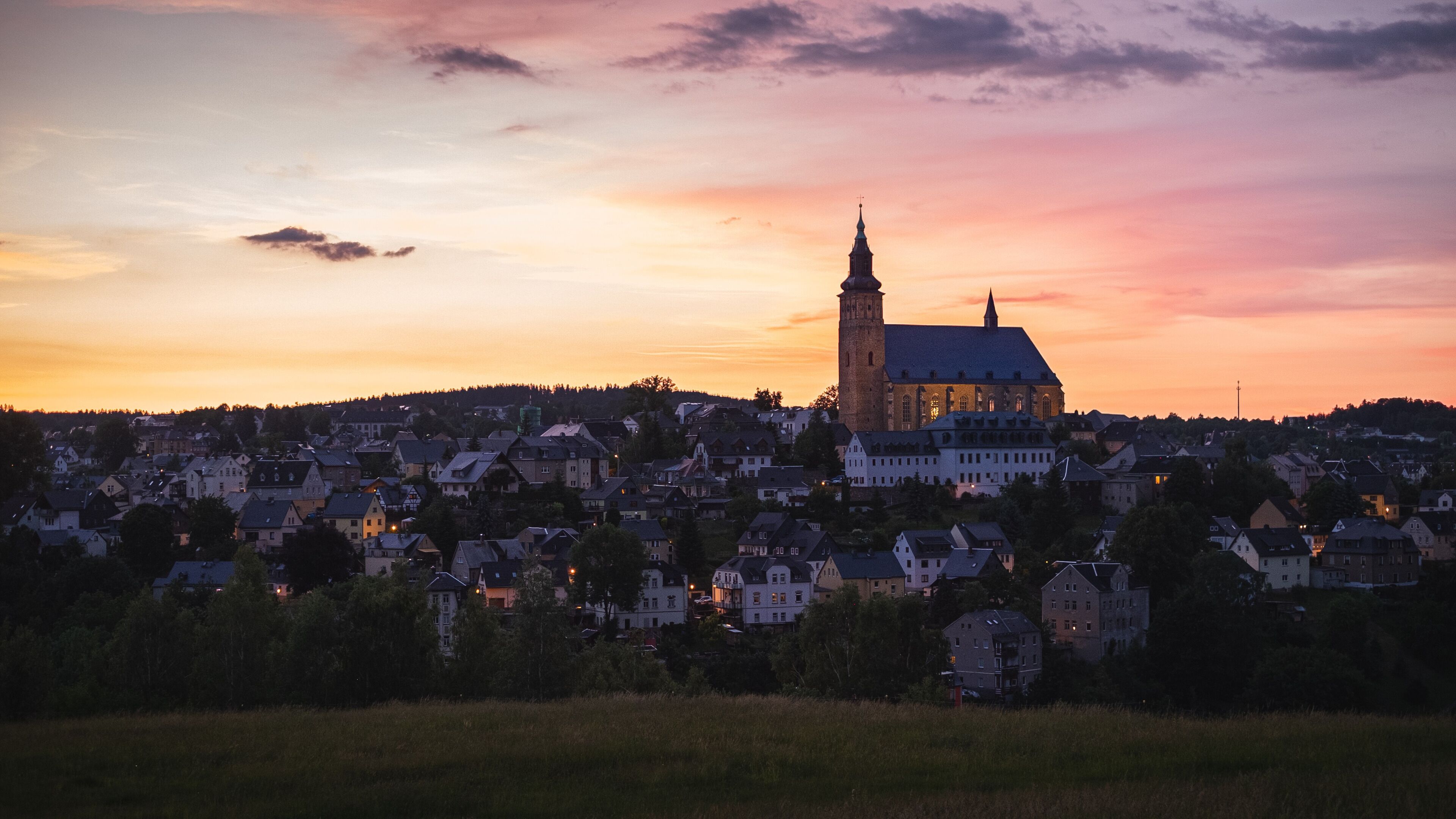 A town with a prominent church tower and a large church building against a sunset sky.