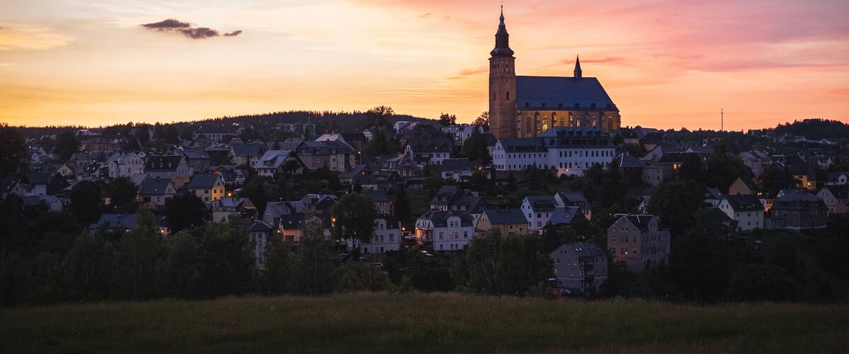 A town with a prominent church tower and a large church building against a sunset sky.