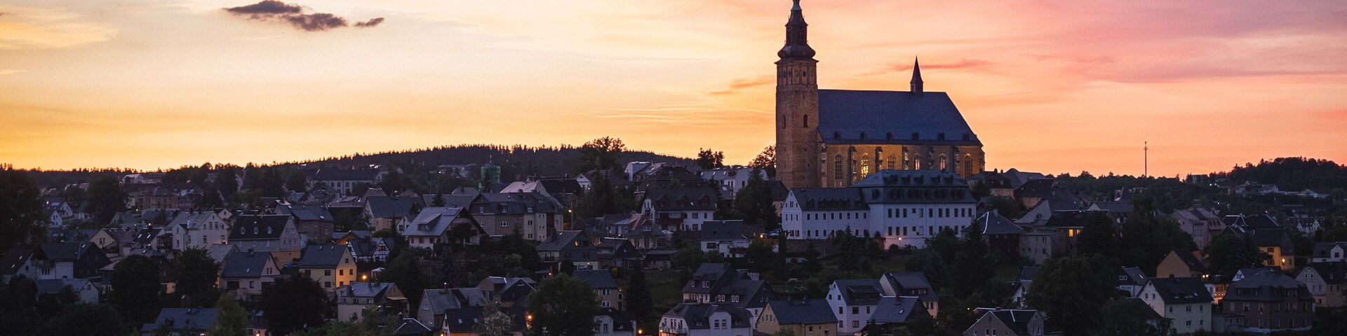A town with a prominent church tower and a large church building against a sunset sky.