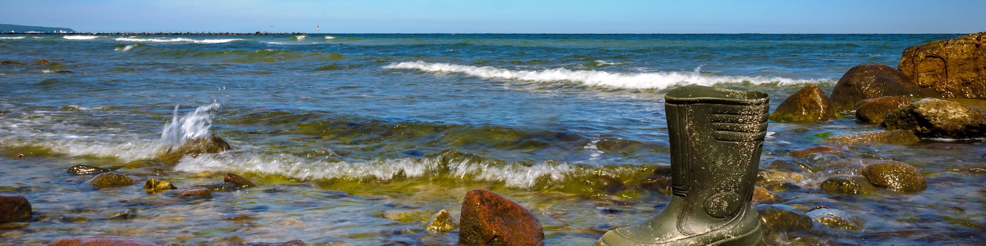 Una costa rocosa con agua cristalina y una bota solitaria en pie sobre una roca.