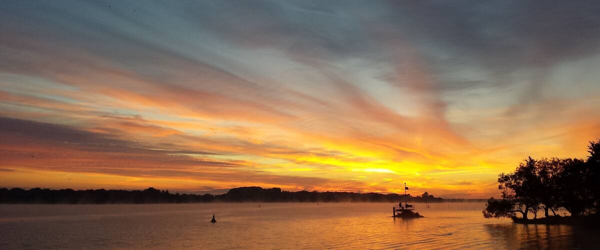 A sunset over a calm body of water with a small boat and a distant shoreline.