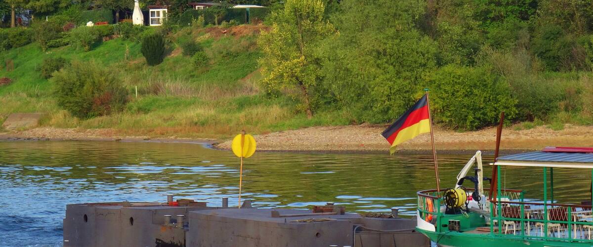 A green and white boat with a German flag on the water.