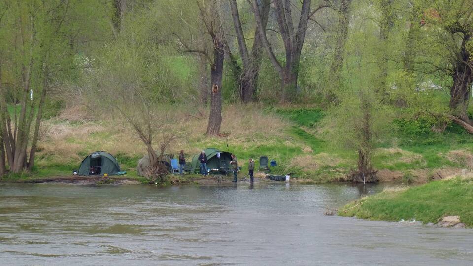 A riverbank with tents and people fishing.