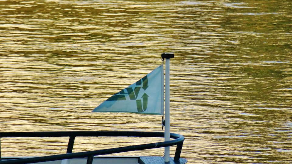 A boat with a triangular flag on a calm body of water.
