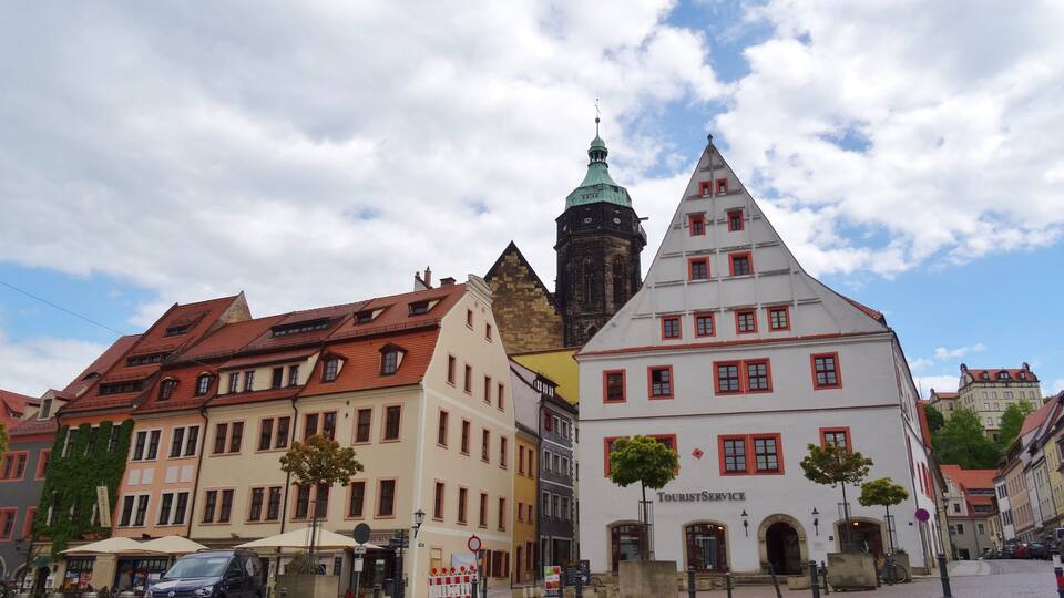A cobblestone square with historic buildings, a church tower, and a tourist service building.