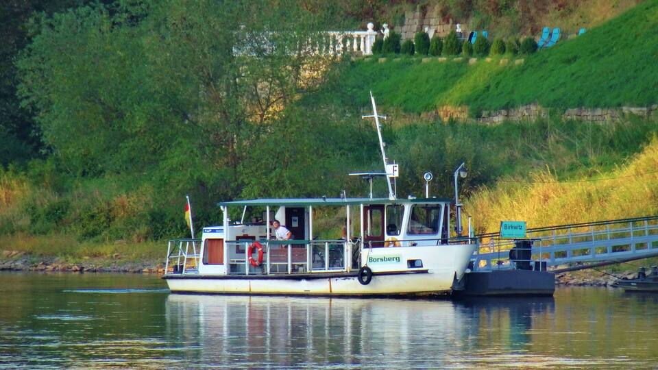 A boat named 'Borsberg' docked near a grassy hillside with a building in the background.