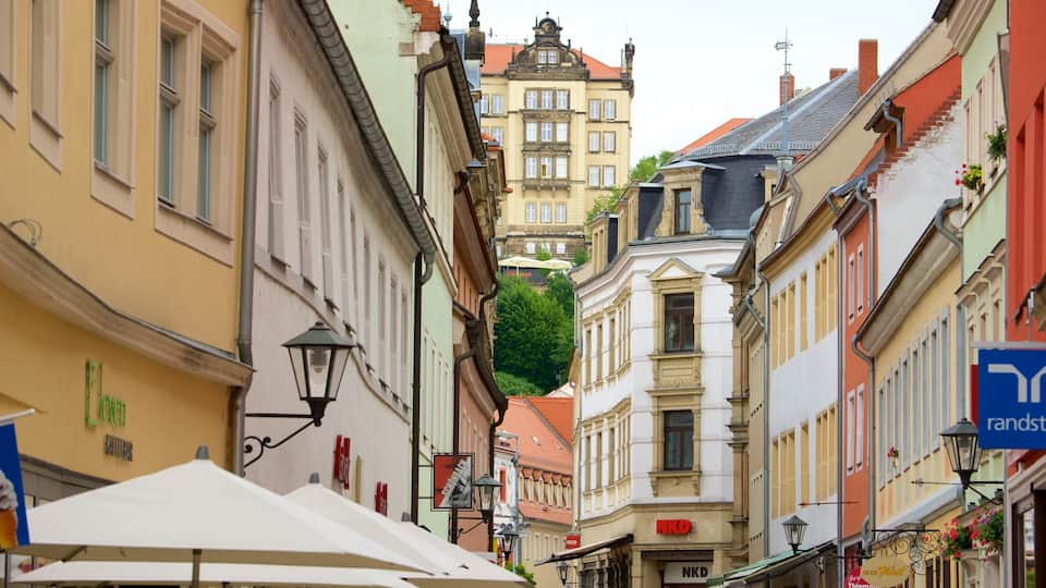 A narrow street lined with colorful buildings, a large tree, and outdoor seating areas.