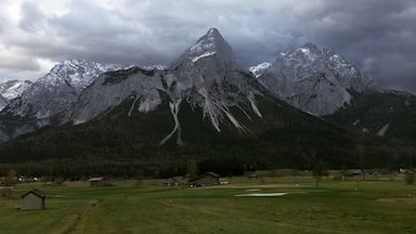 A mountain range with snow-capped peaks, a green valley, and scattered buildings.