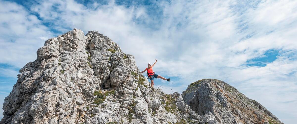 A person climbing a rocky mountain peak with a clear sky in the background.