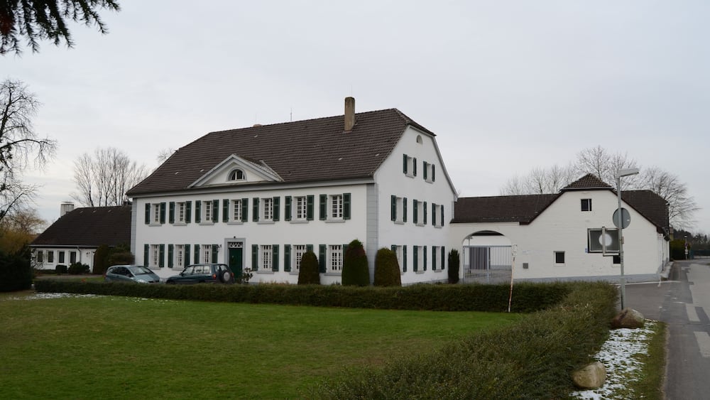 Ein großes weißes Haus mit grünen Fensterläden, einer Garage und einer Auffahrt mit parkenden Autos.