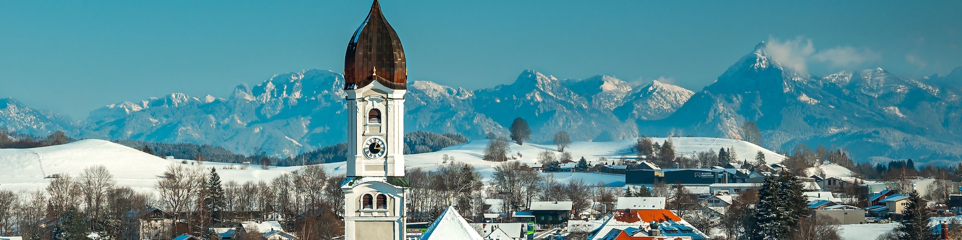 Un pueblo cubierto de nieve, con una iglesia destacada y montañas al fondo.
