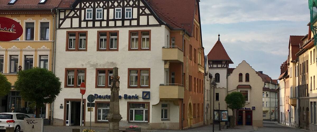 A cobblestone square with historic buildings, a statue, and a bank.