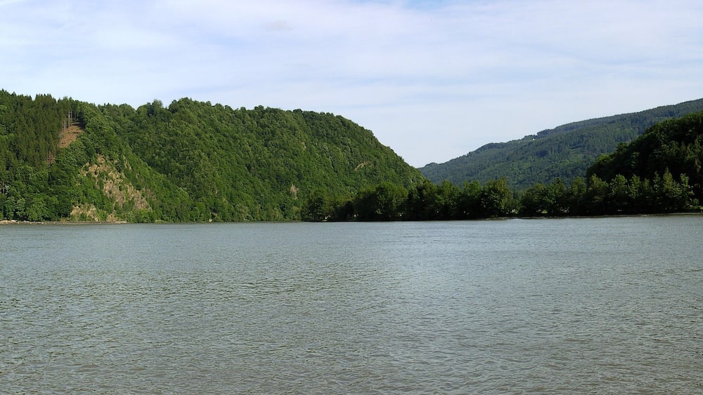 Ein ruhiger See, umgeben von dichten Wäldern und Hügeln.