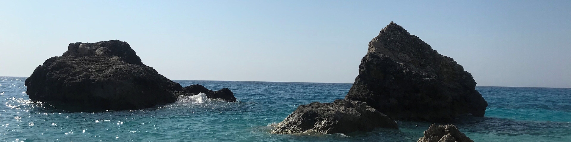 A beach with pebbly shore, clear blue sea, and rocky formations.