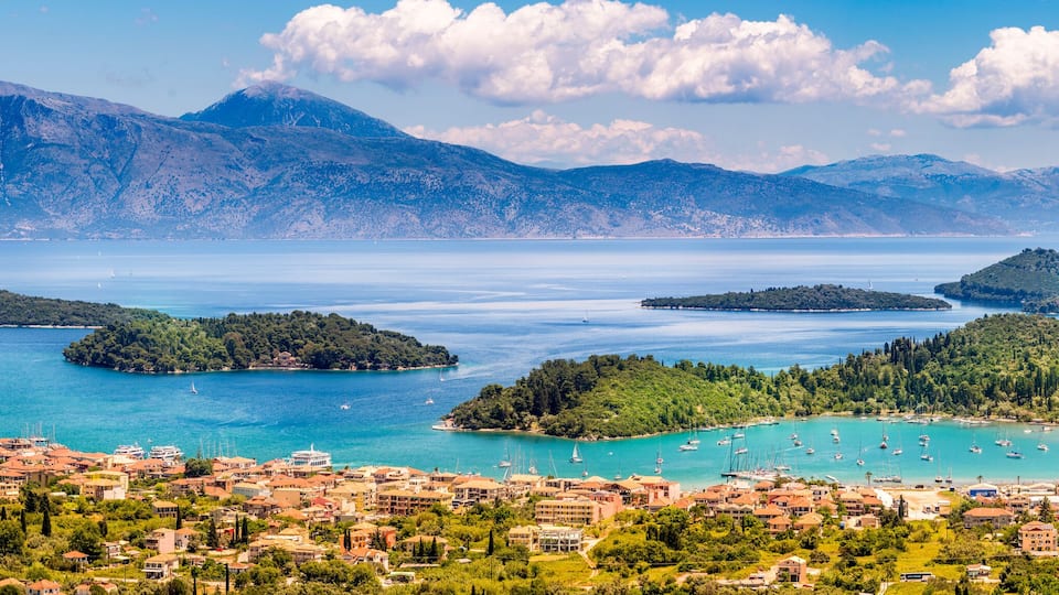 A coastal town with a marina, surrounded by mountains and clear blue waters.
