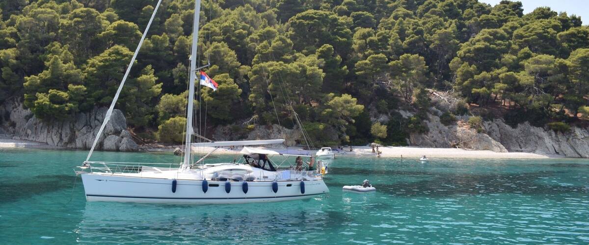 A sailboat on turquoise waters with a forested hill in the background.