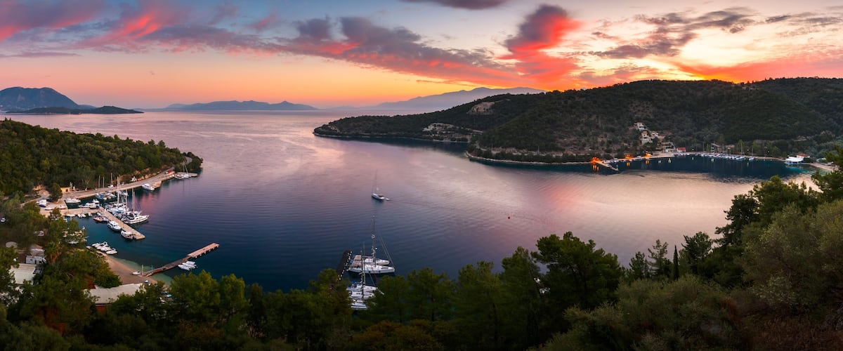 A coastal landscape with a marina, boats, and a sunset over the water.