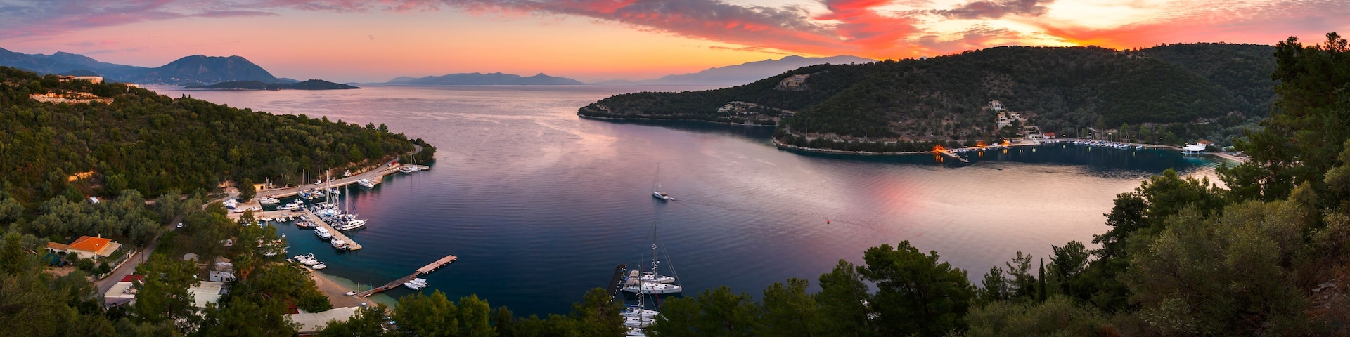 A coastal landscape with a marina, boats, and a sunset over the water.