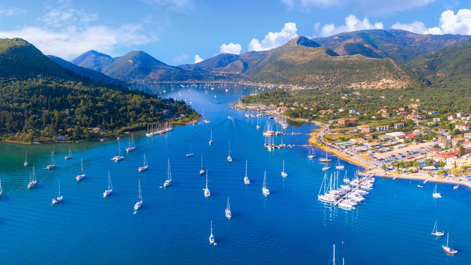 A coastal town with a marina filled with sailboats, surrounded by lush green hills and mountains.
