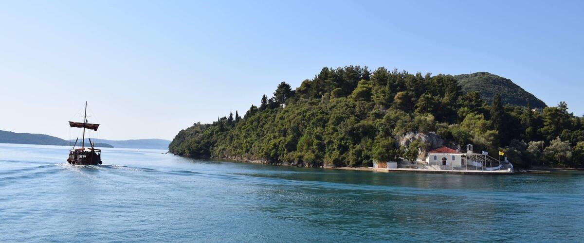 A boat on a calm lake with a small island covered in trees and a building with a red roof.
