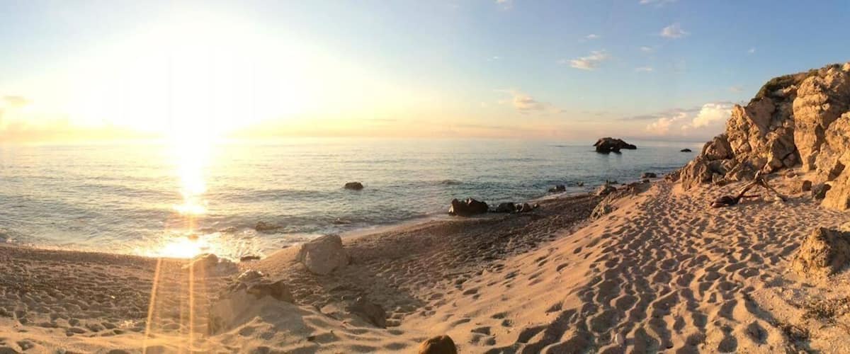 A beach with a person walking, rocky cliffs, and the ocean.