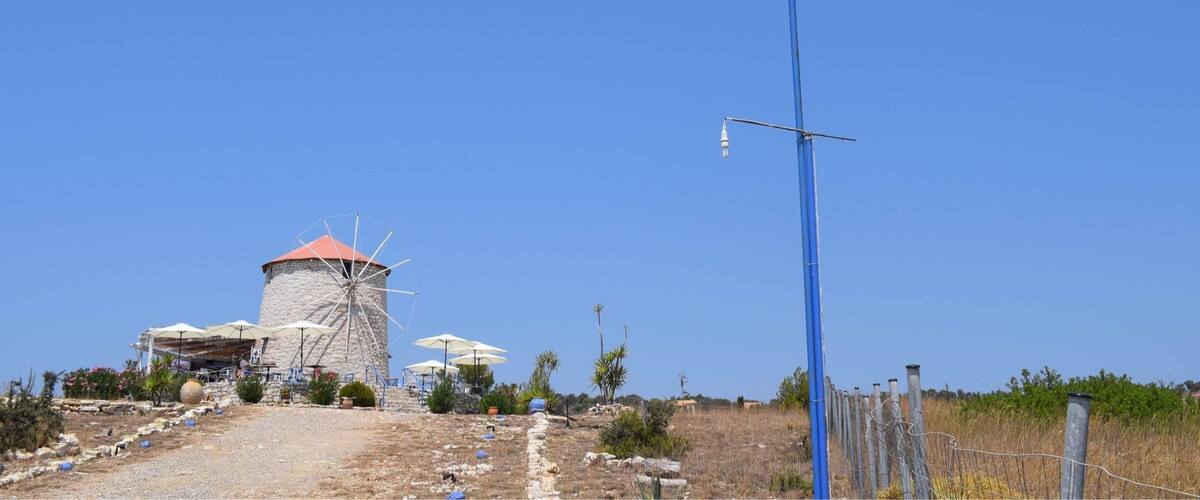 A windmill, a flagpole with a flag, and a building with umbrellas.