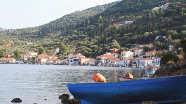 A coastal village with houses on a hillside, a calm sea, and a blue boat on the shore.