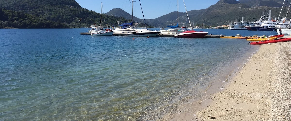A calm lake with several sailboats docked along the shore, surrounded by hills.