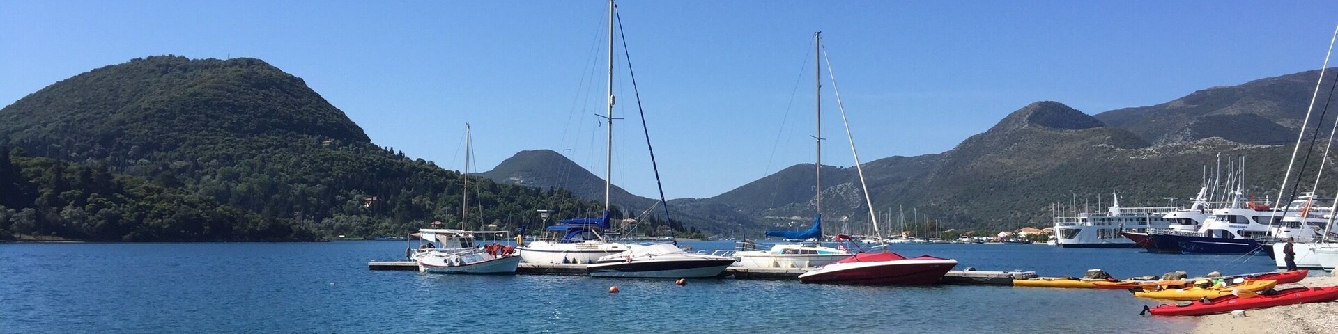 A calm lake with several sailboats docked along the shore, surrounded by hills.