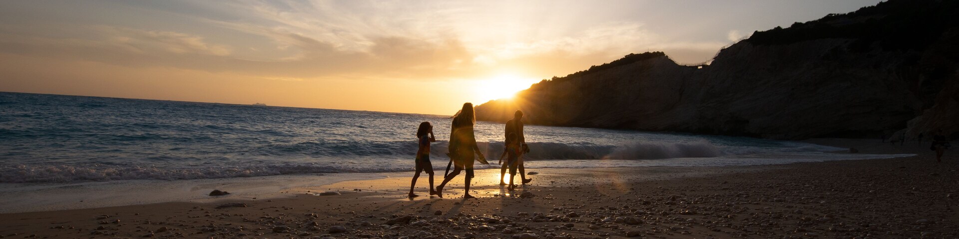 Una playa con gente caminando por la orilla al atardecer.