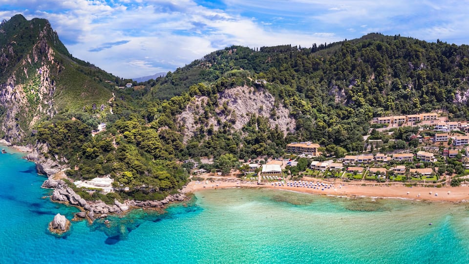 A coastal town with a mountain, clear turquoise waters, and a sandy beach.