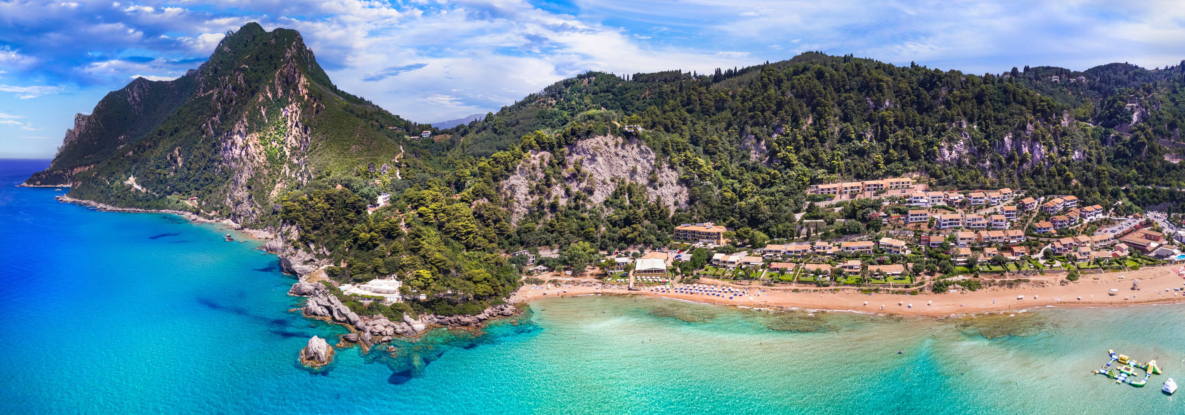 A coastal town with a mountain, clear turquoise waters, and a sandy beach.