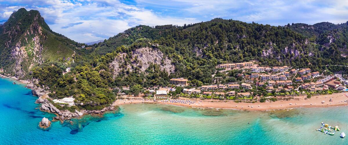 A coastal town with a mountain, clear turquoise waters, and a sandy beach.