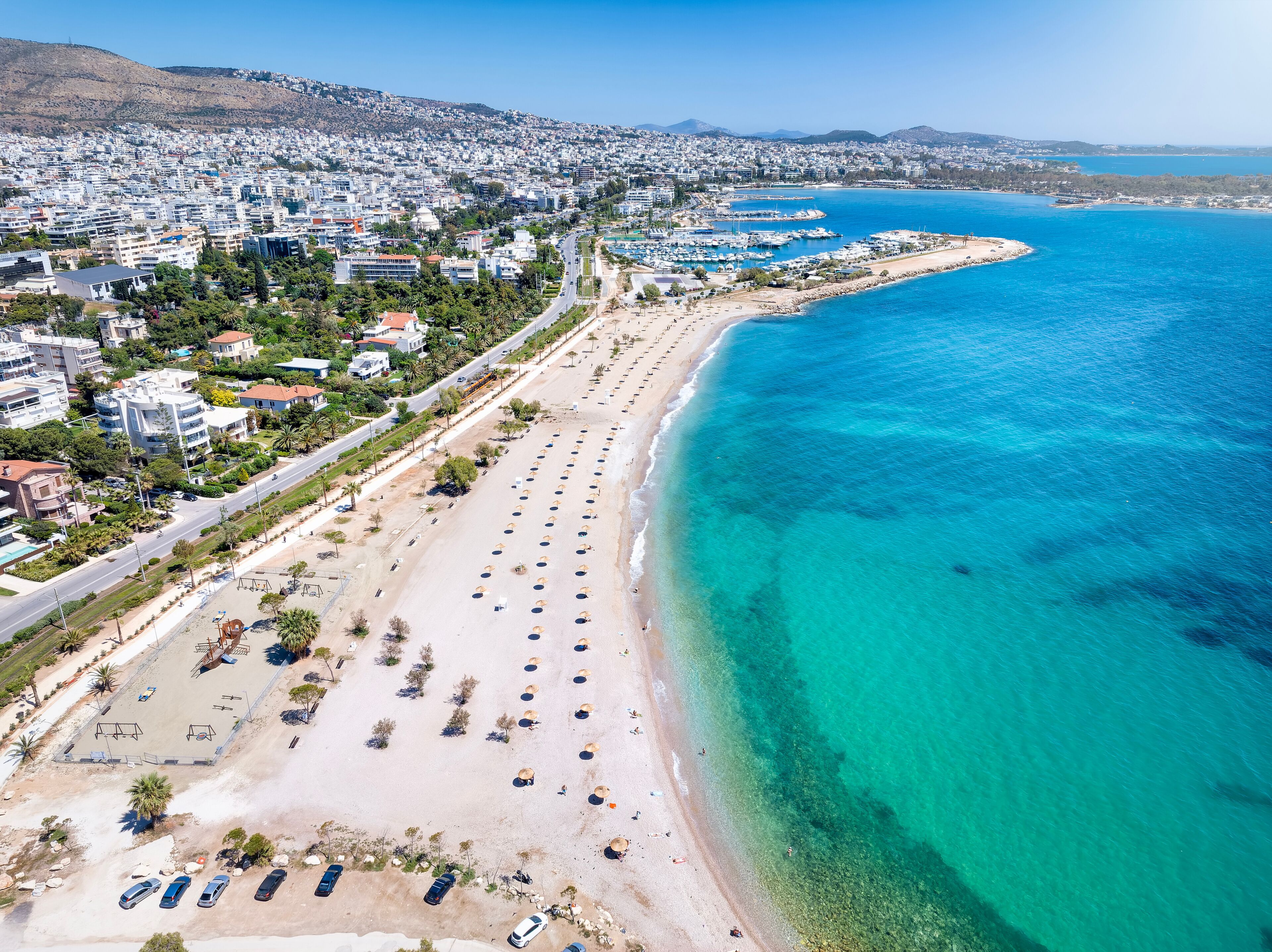 A coastal cityscape with a long sandy beach, a marina, and dense urban buildings.