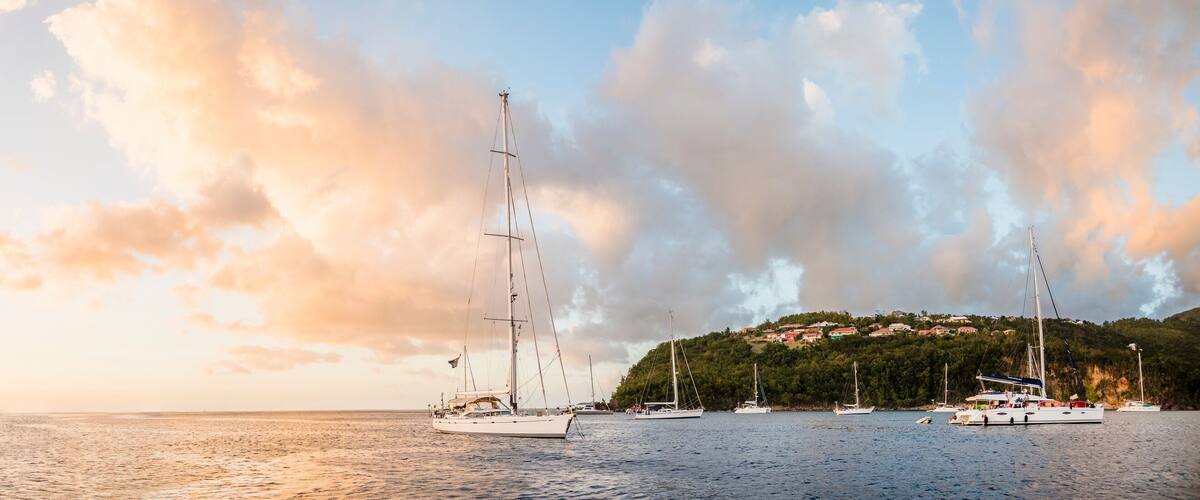 A coastal scene with sailboats, a distant island, and a hill with buildings.