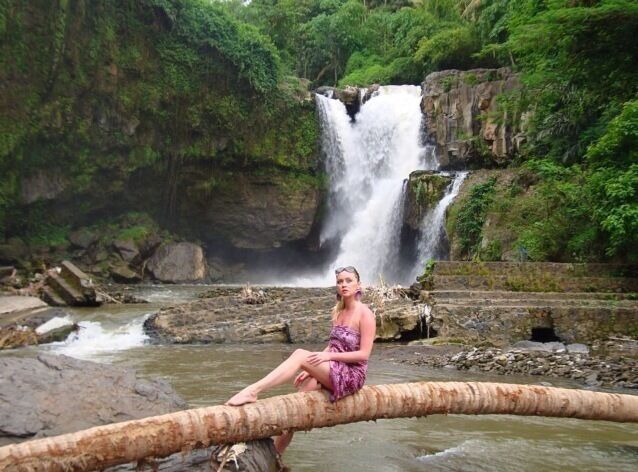 A waterfall, a person sitting on a log, and a river.