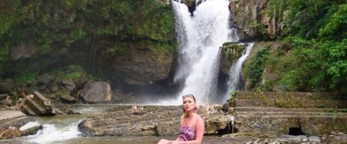 A waterfall, a person sitting on a log, and a river.