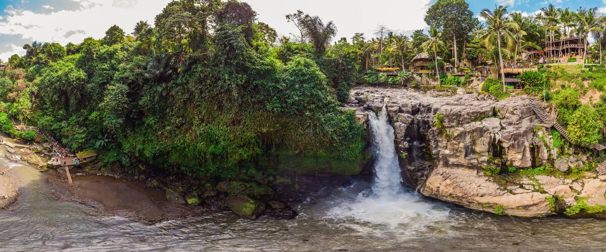 A waterfall cascading over a rocky cliff surrounded by lush greenery and a beach.