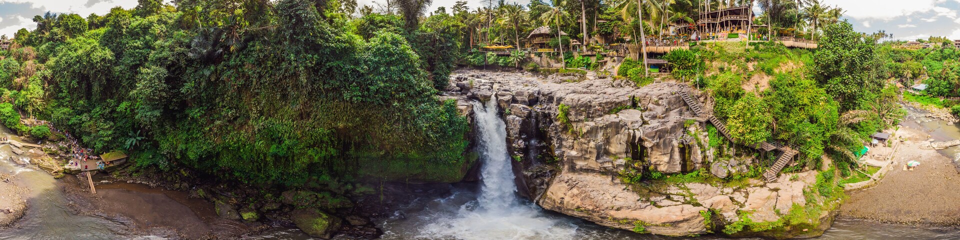 A waterfall cascading over a rocky cliff surrounded by lush greenery and a beach.