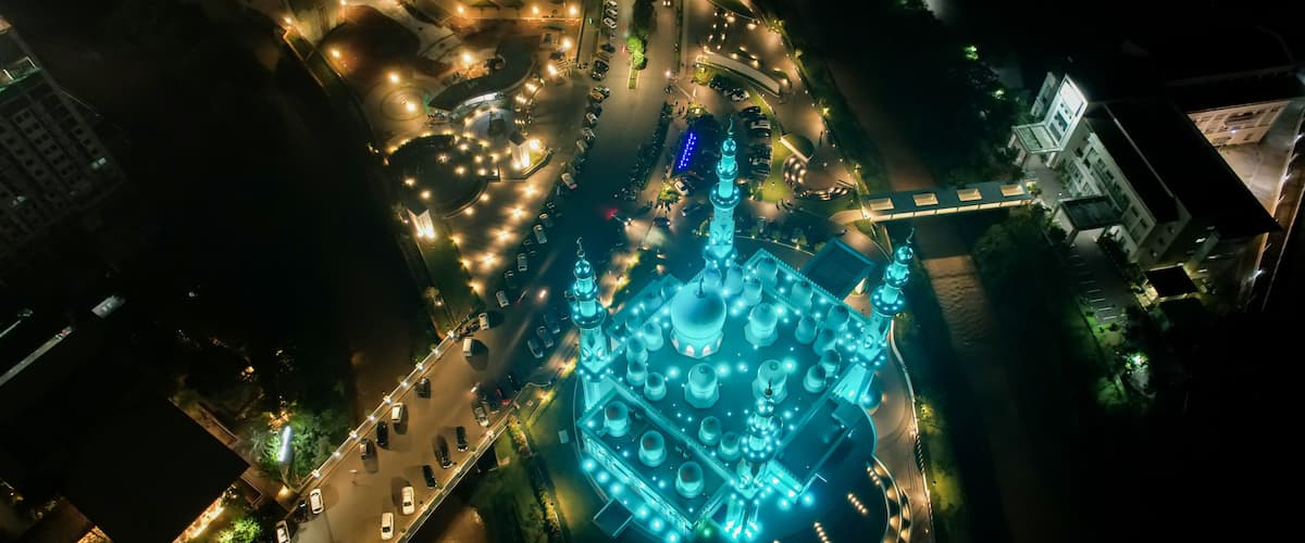 An aerial view of a cityscape at night with a prominent mosque illuminated by blue lights.