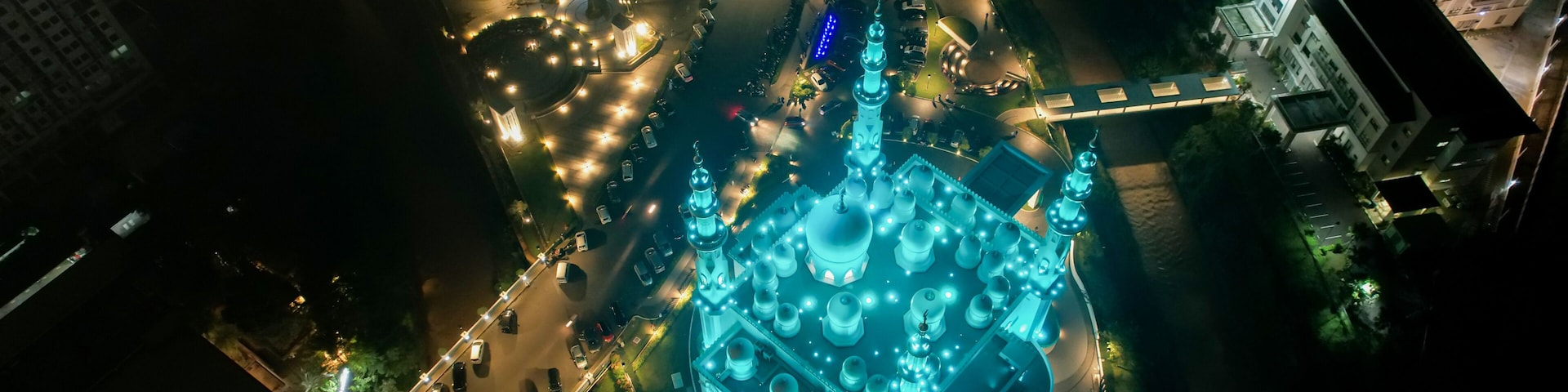An aerial view of a cityscape at night with a prominent mosque illuminated by blue lights.
