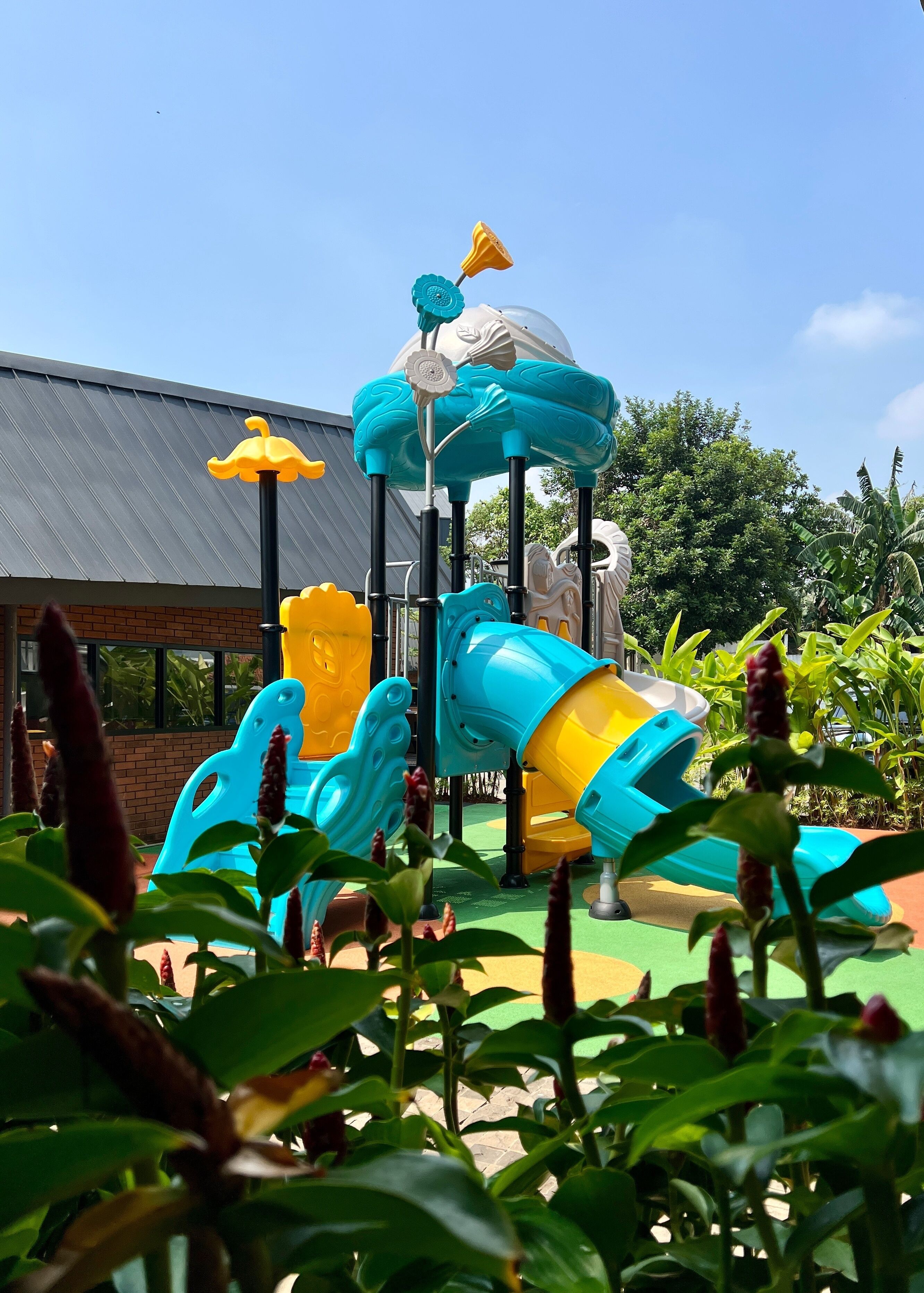 A playground with a blue and yellow slide, surrounded by greenery.
