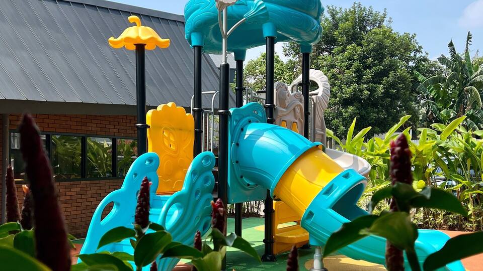 A playground with a blue and yellow slide, surrounded by greenery.