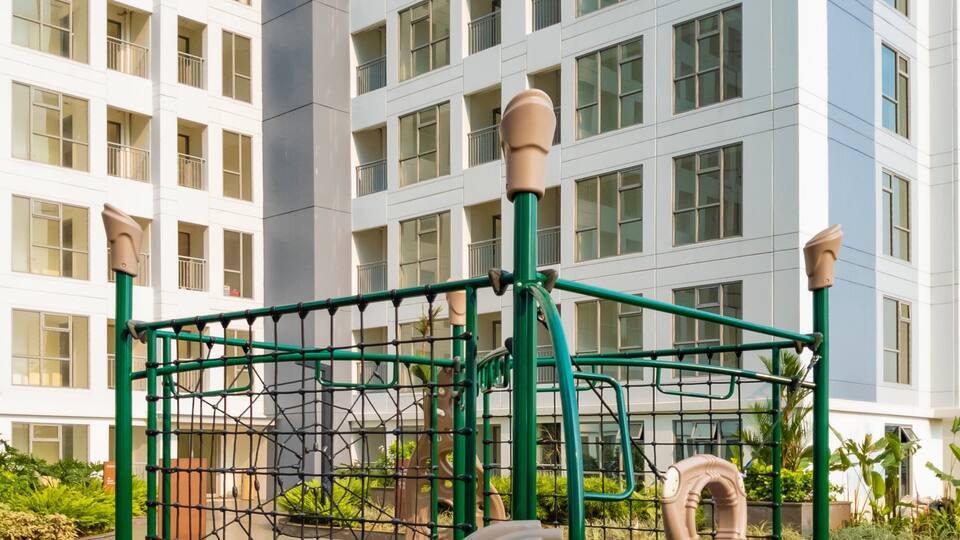 A playground with a slide and climbing net, surrounded by a building with multiple windows.