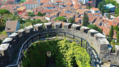 A historic stone wall with a circular courtyard, surrounded by a cityscape with red-roofed buildings and a distant mountain range.