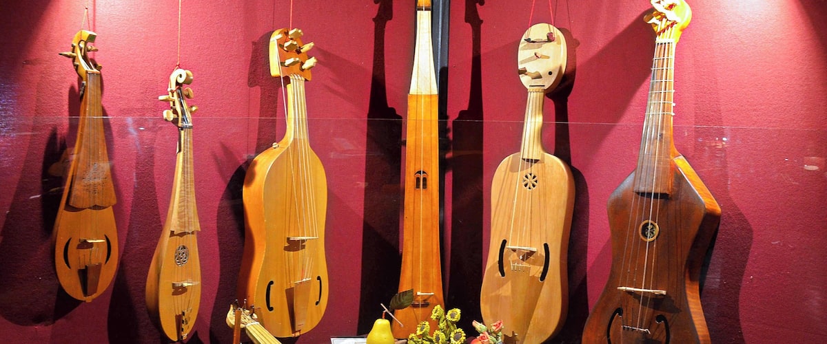 A display of various stringed musical instruments, including guitars and lutes, on a red background with a framed document and decorative items.