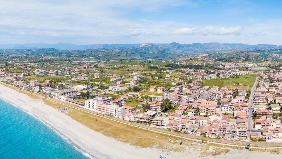 A coastal city with a beach, residential areas, and rolling hills in the background.